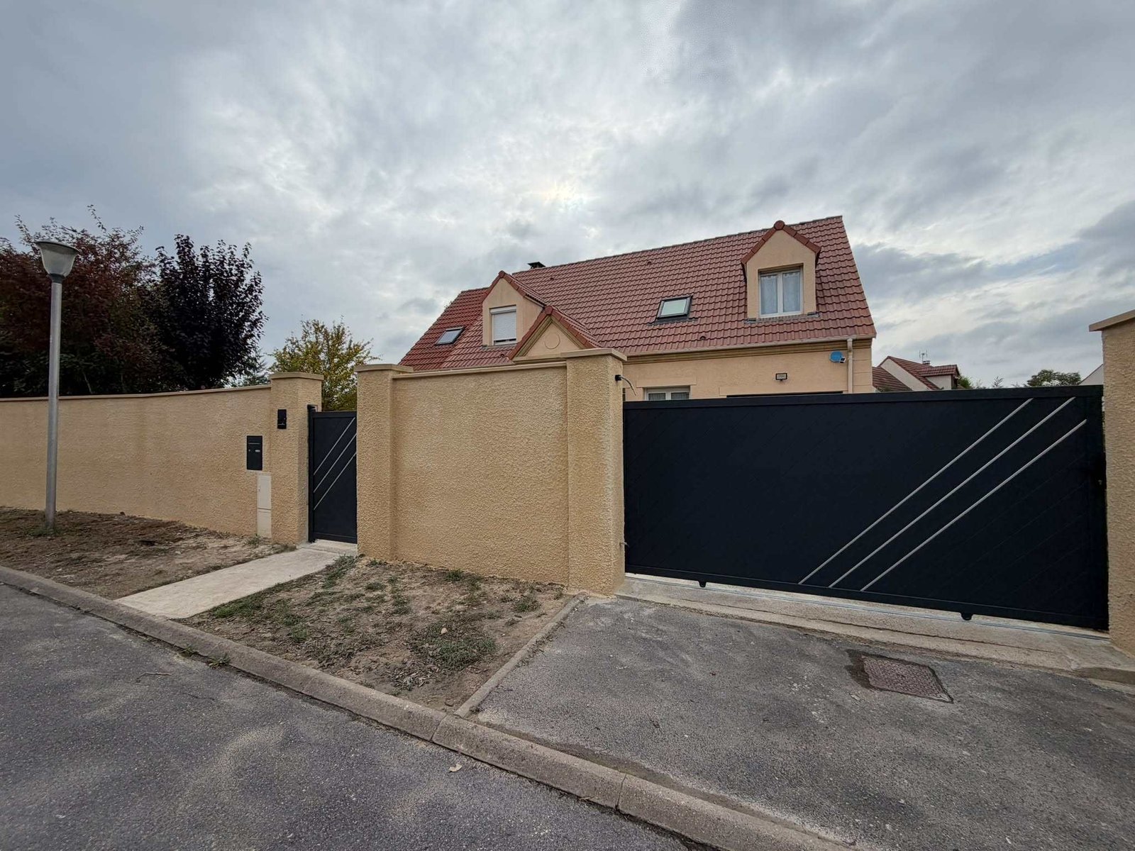 Mur de clôture enduit, portail coulissant et portillon devant une maison