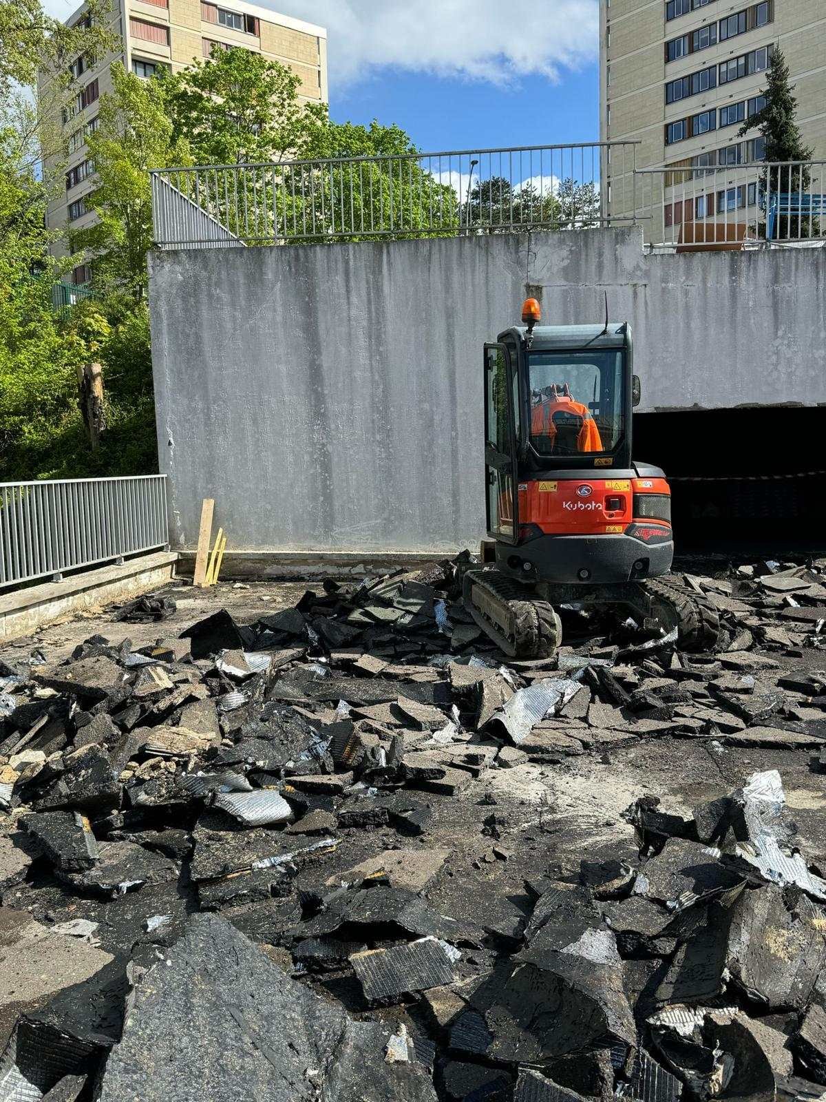 Mini-pelle en cours de démolition d’une dalle, au pied d’immeubles