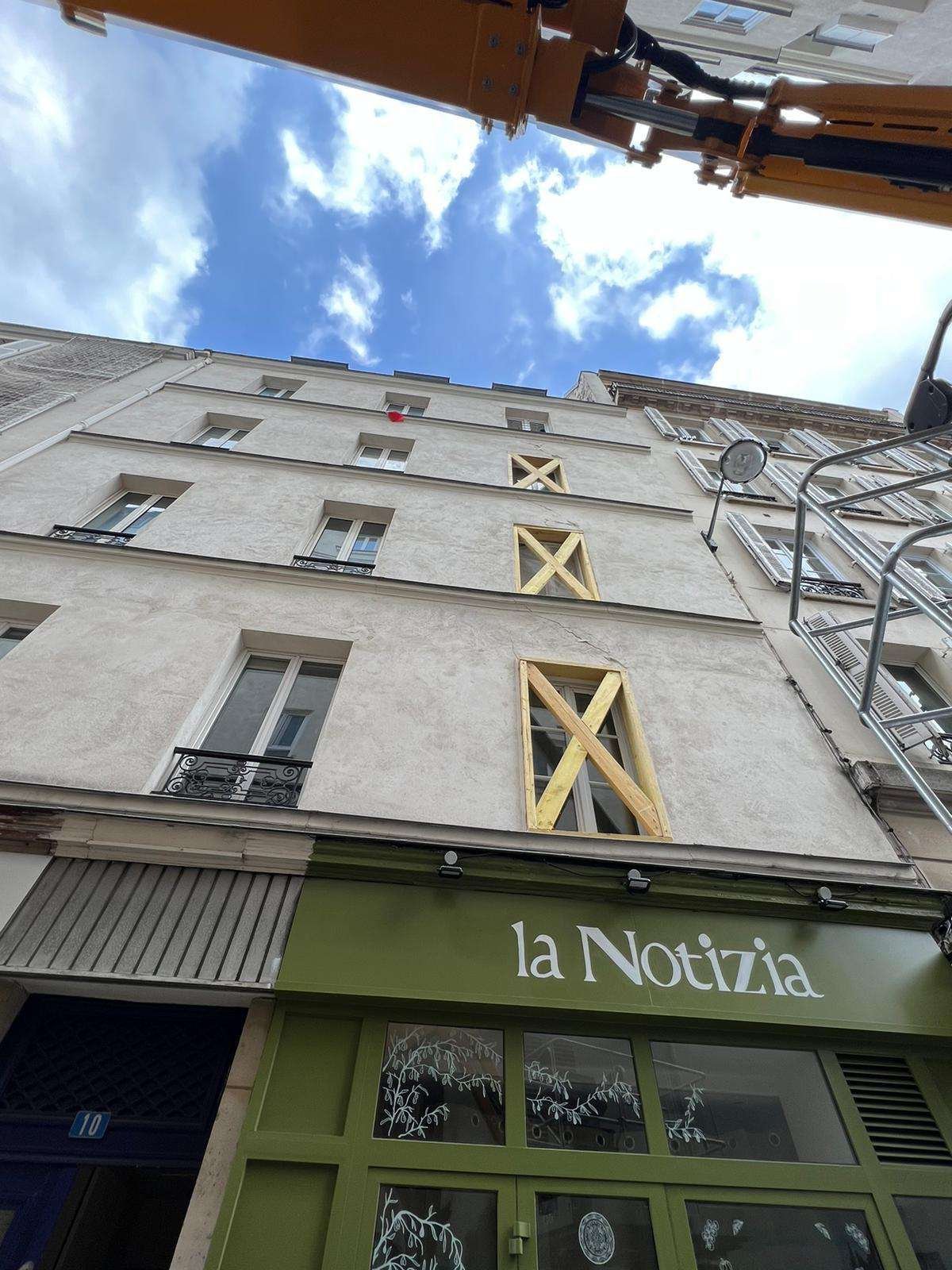 Façade d’immeuble aux fenêtres étrésillonnées par des étais en bois en croix, nacelle élévatrice en position