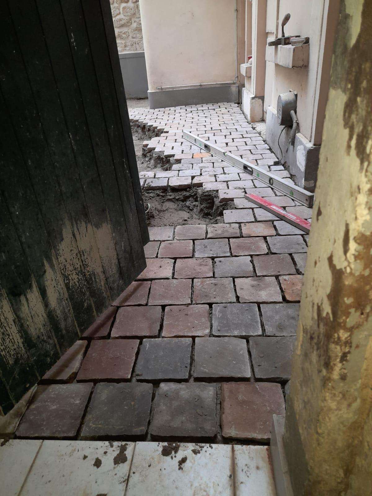 Pose de pavés en cours dans un passage étroit entre deux bâtiments